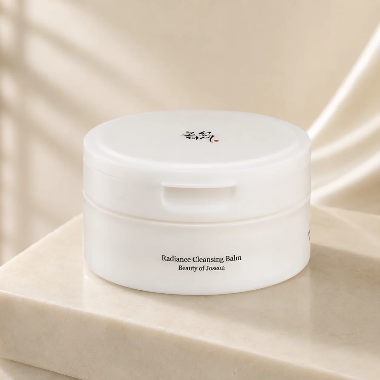 White tub of Beauty of Joseon Radiance Cleansing Balm on a beige marble surface with soft lighting.